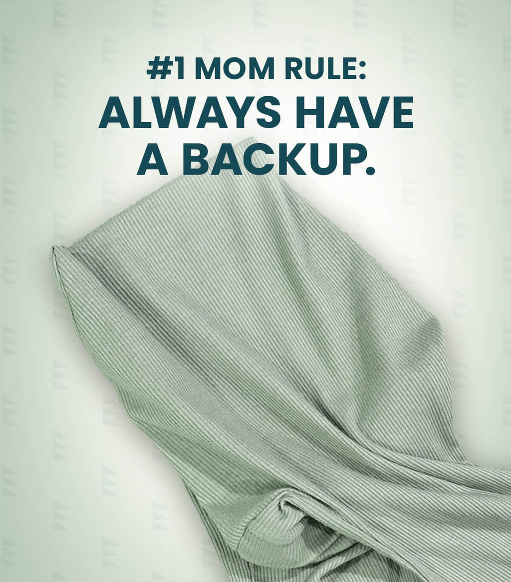 Acute Baby Co. folded ribbed knit garment in a pale sage green color, shown with a dark teal text overlay that reads '#1 MOM RULE: ALWAYS HAVE A BACKUP.' on a light off-white background with a subtle repeating watermark pattern.