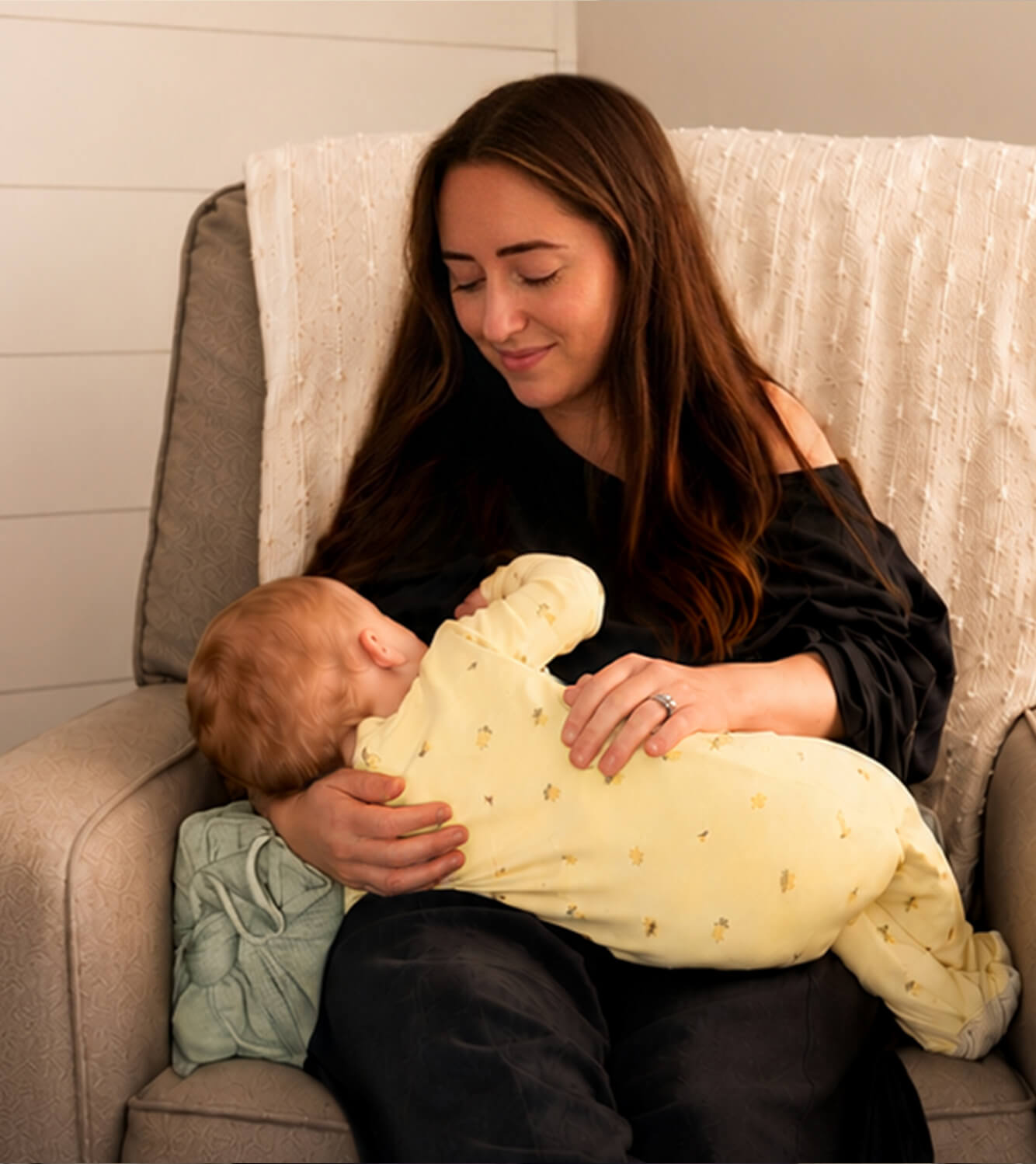 A Woman breastfeeding baby using the Acute Baby Co. Wedge under her arm for adding wrist, hand, and arm support while nursing. 
