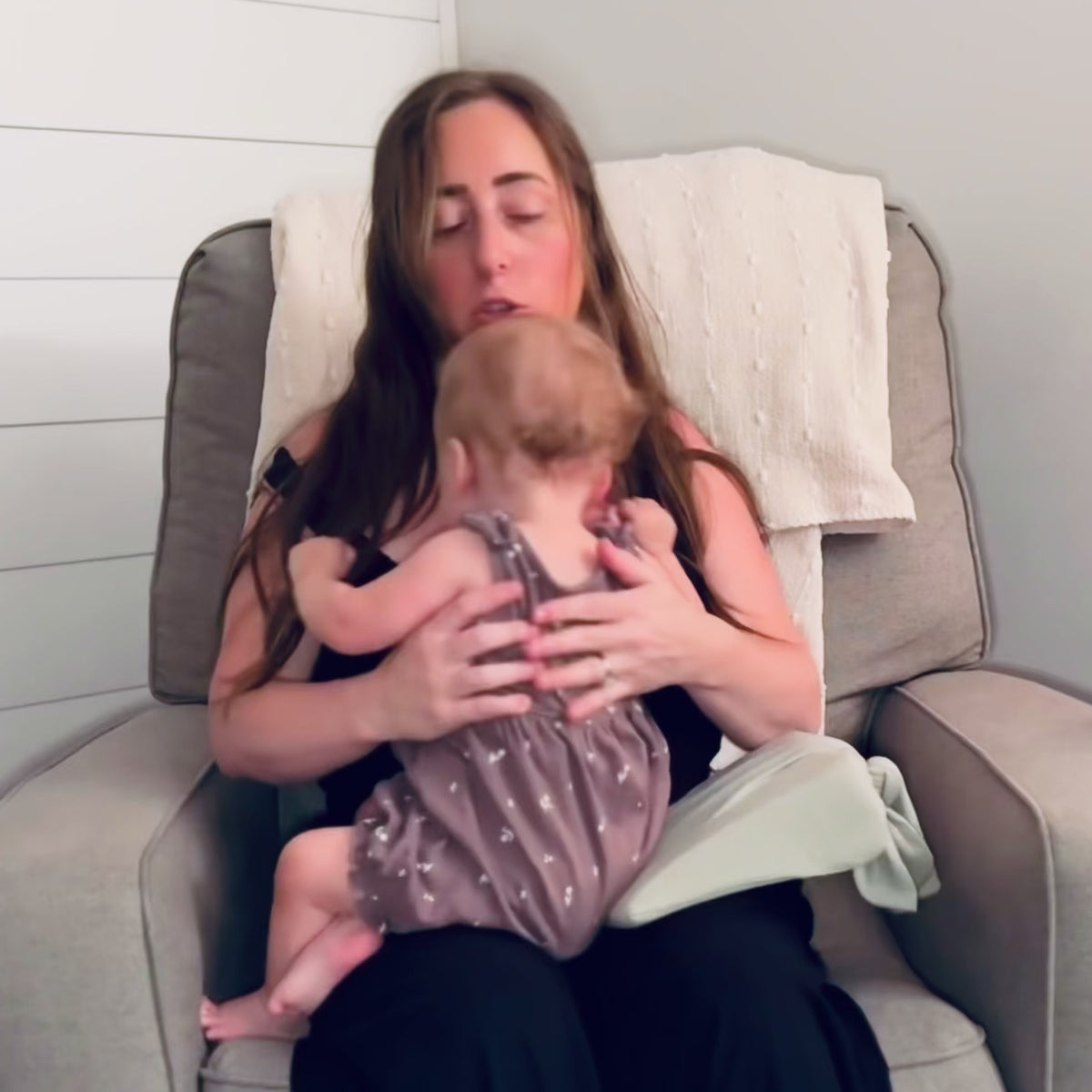 A woman showcasing how to breastfeed a baby with the Acute Baby Co Wedge under the baby's head for added support, height, and comfort. 